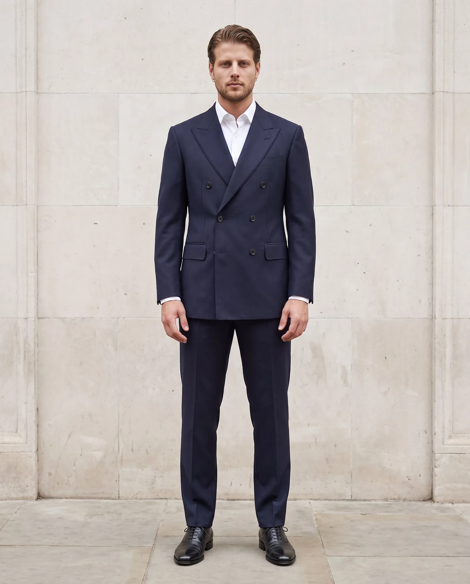 Model in a navy double-breasted suit against pale stone